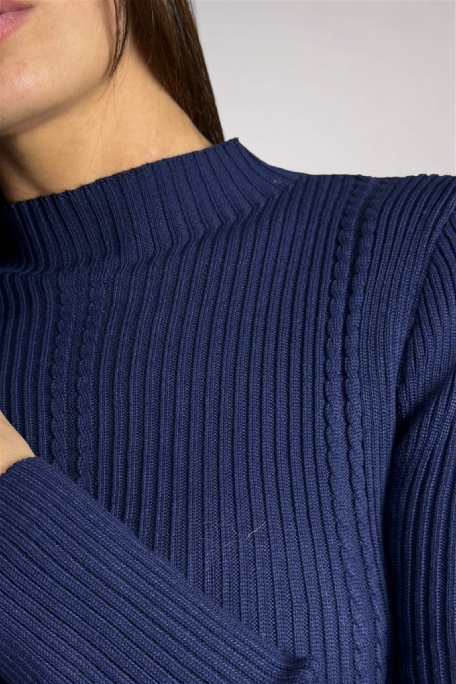 Close-up of a person wearing a blue ribbed sweater with a plain background