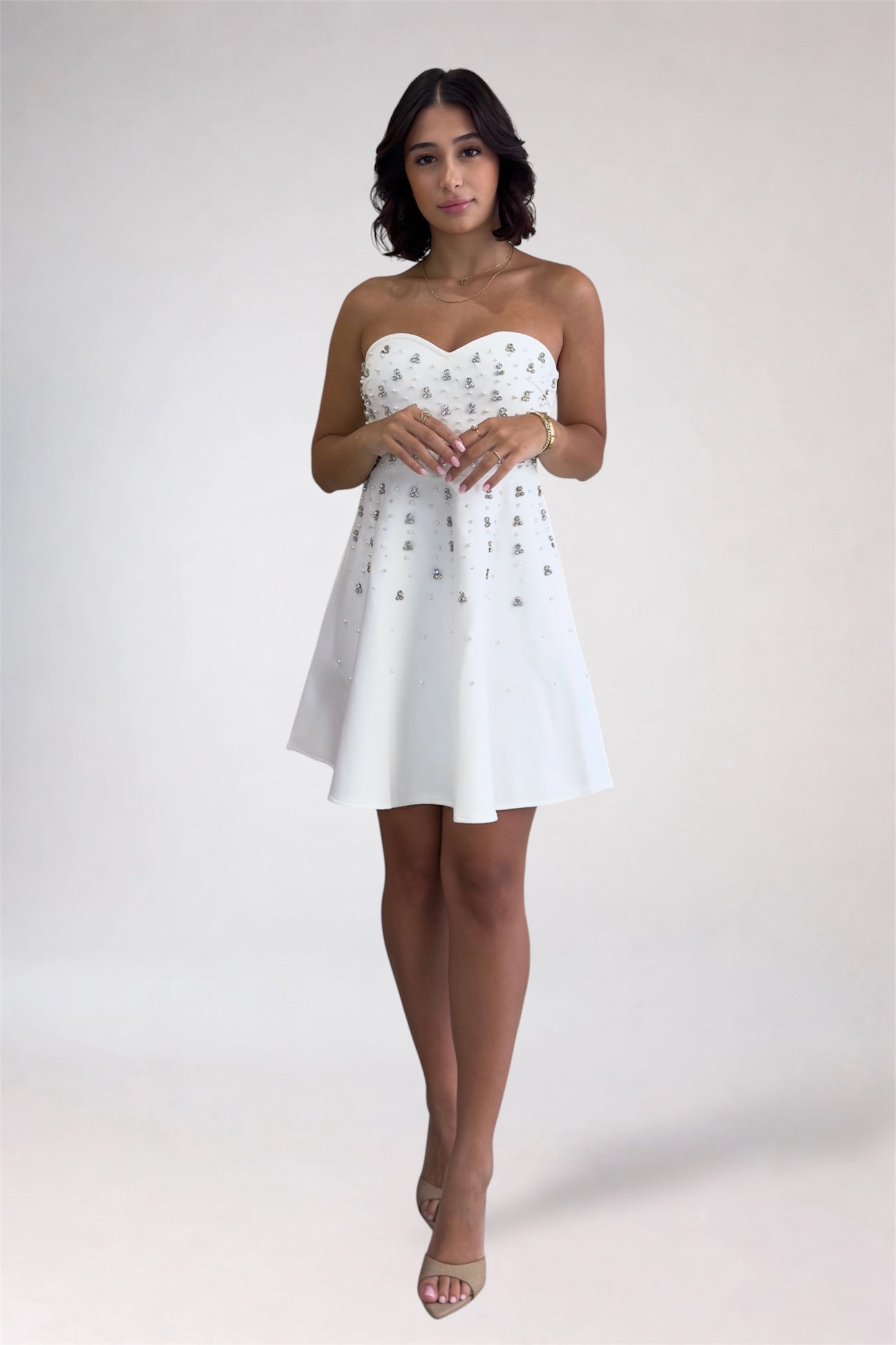 Woman wearing a white strapless dress with gold embellishments on a plain background