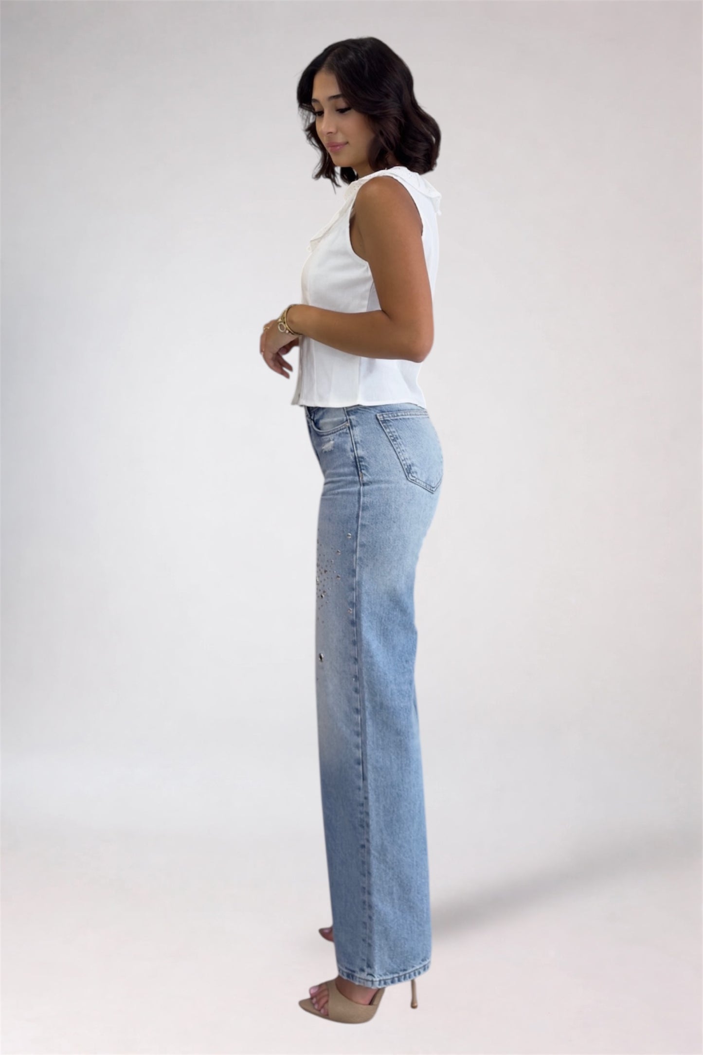 Woman wearing light blue jeans and a white top on a plain background