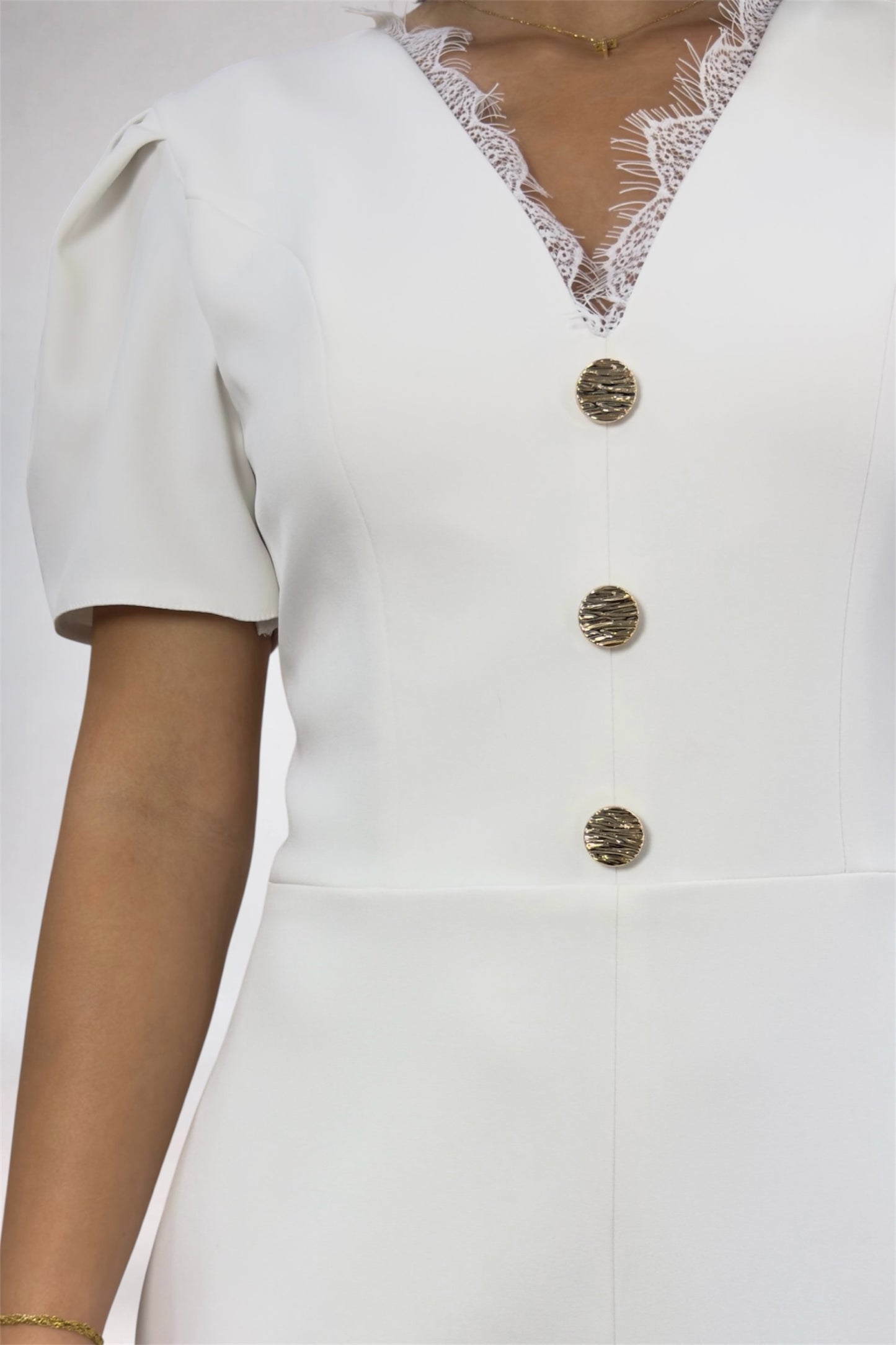 White outfit with gold buttons and lace details on a plain background