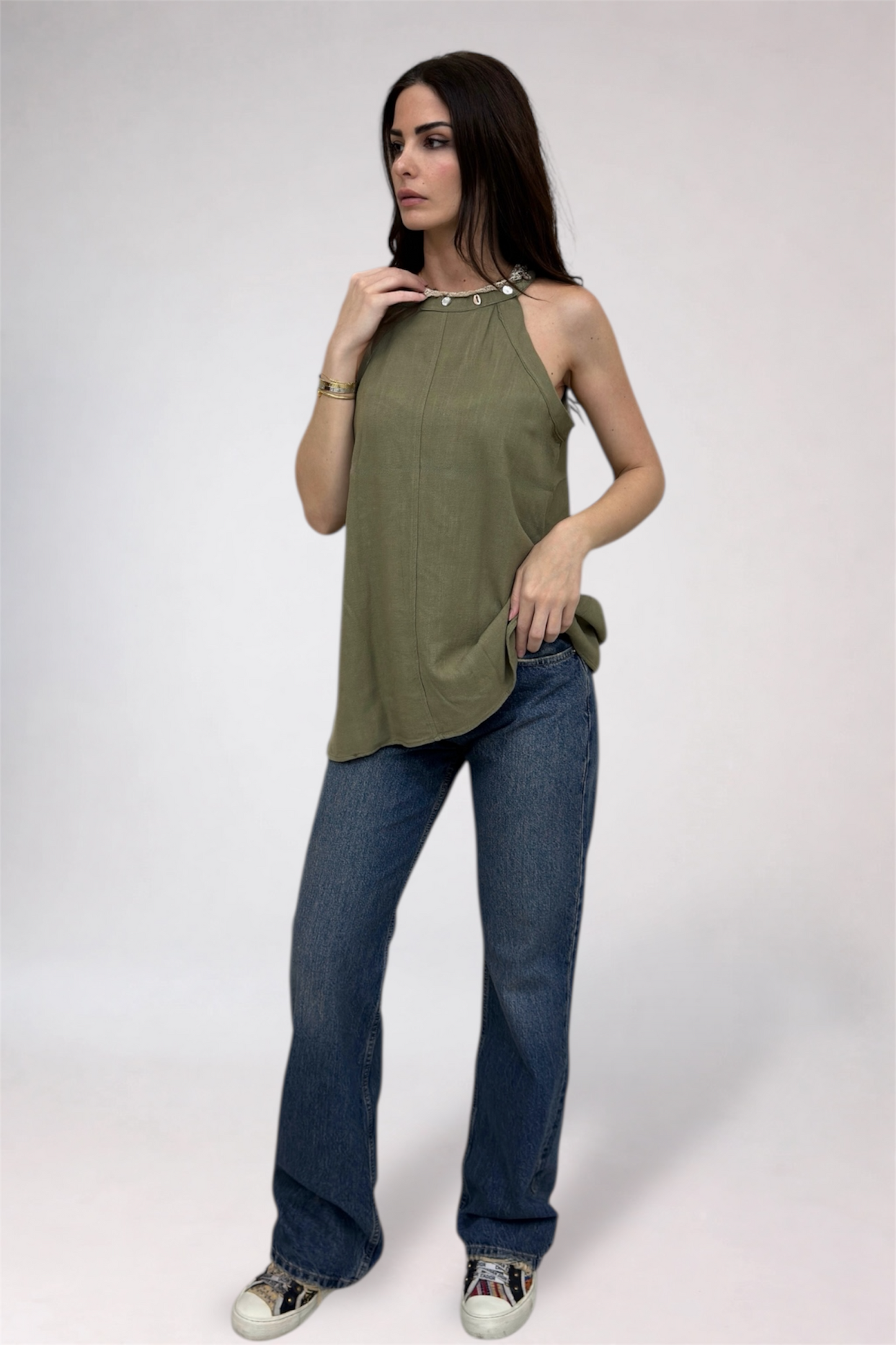 Woman wearing a green sleeveless top and blue jeans on a white background
