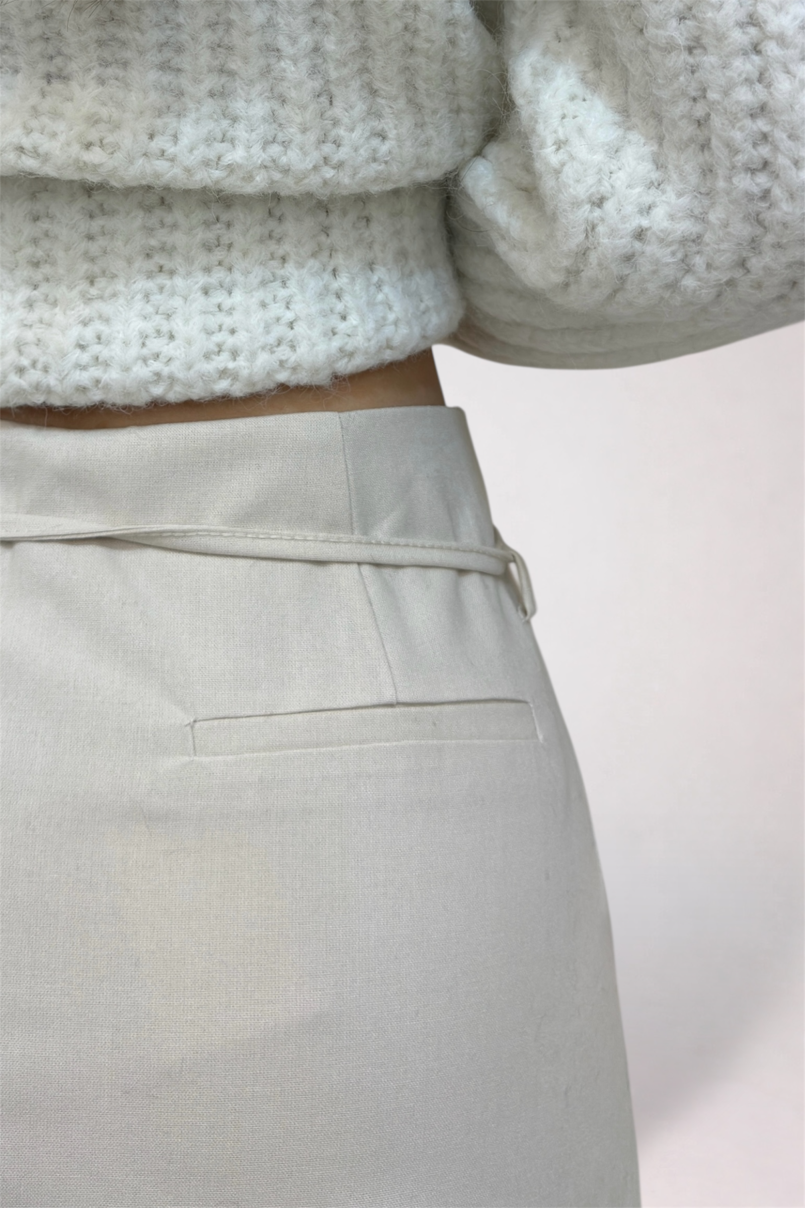 Close-up of a person wearing a textured sweater and light-colored pants on a plain background