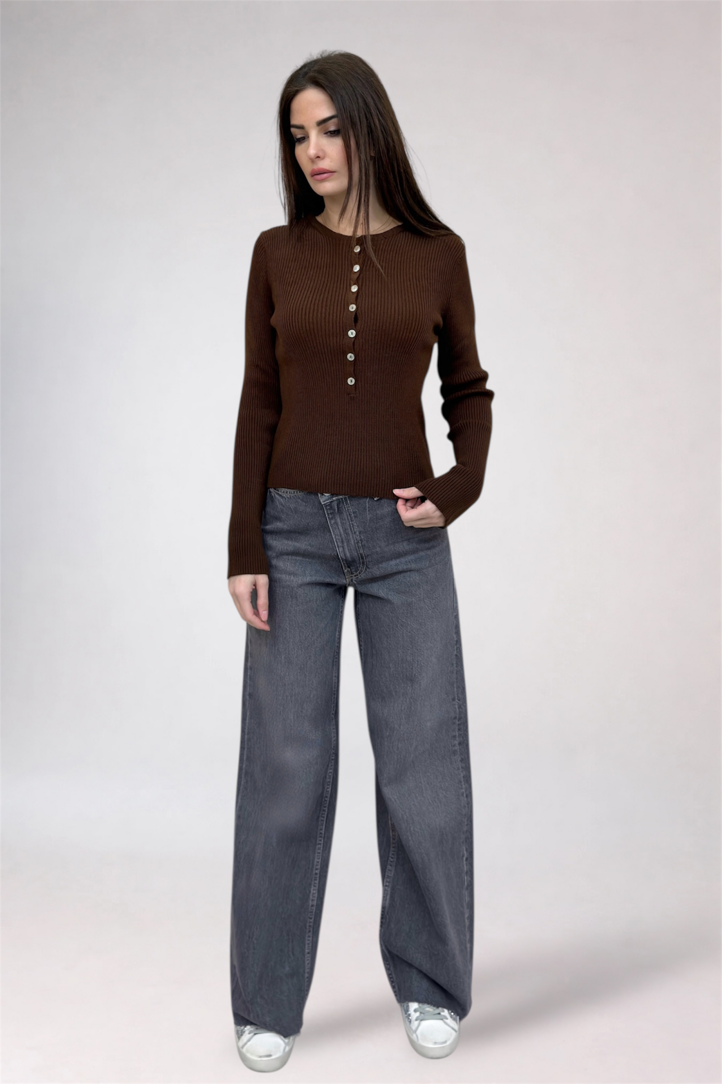 Woman wearing a brown button-up shirt and gray jeans on a white background