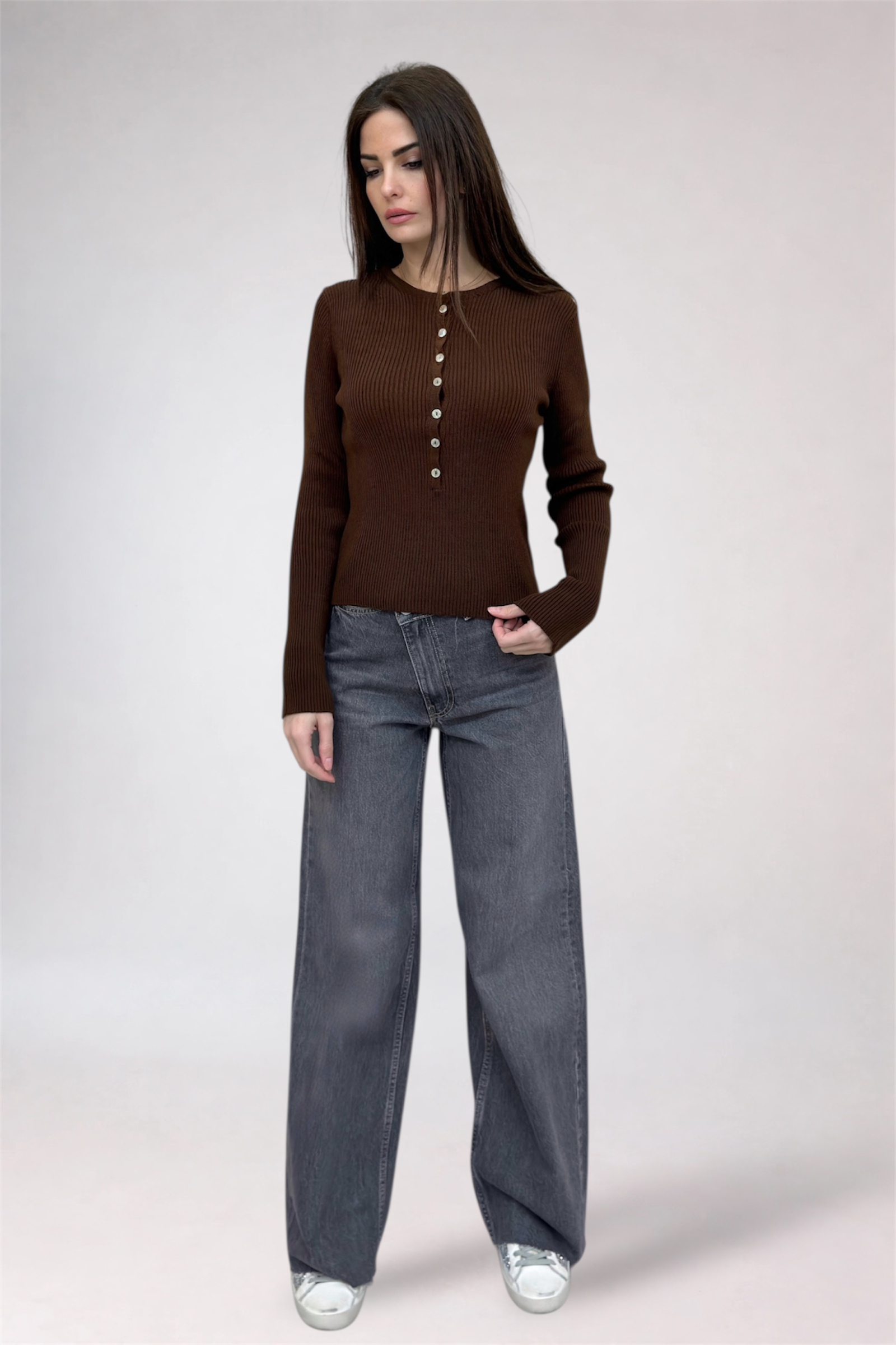 Woman wearing a brown button-up shirt and gray jeans on a white background