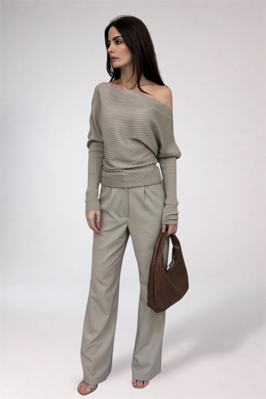 Woman wearing a beige off-shoulder top and pants with a brown handbag on a white background