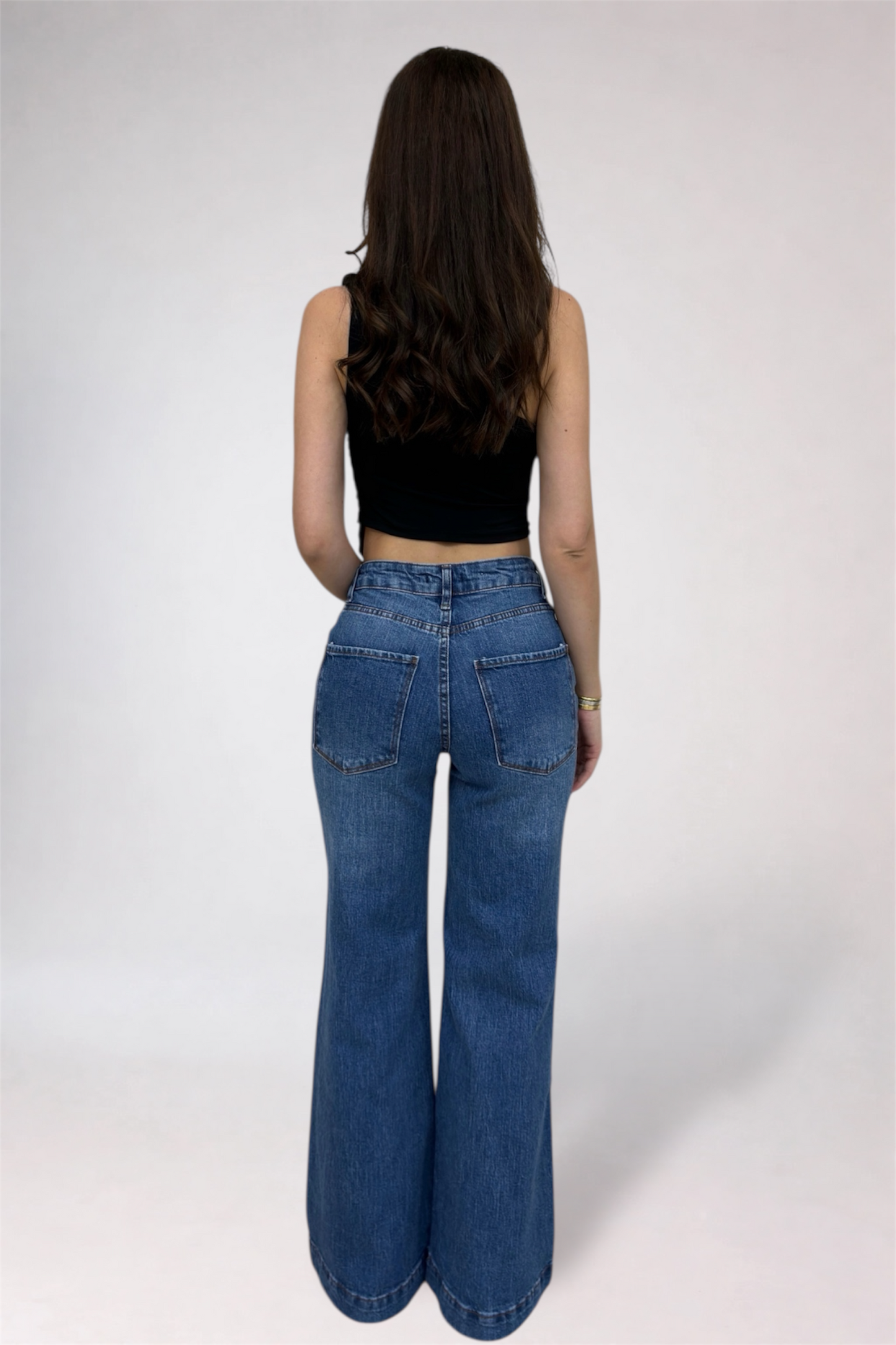 Person wearing blue jeans and a black top on a white background