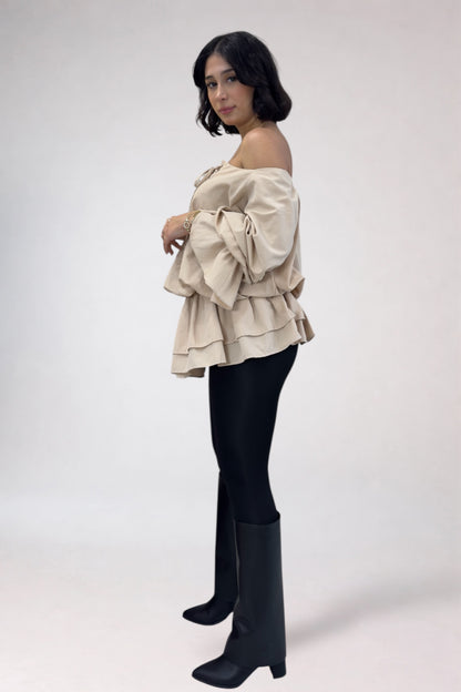 Woman wearing a beige off-shoulder ruffled top and black leggings with knee-high boots on a white background