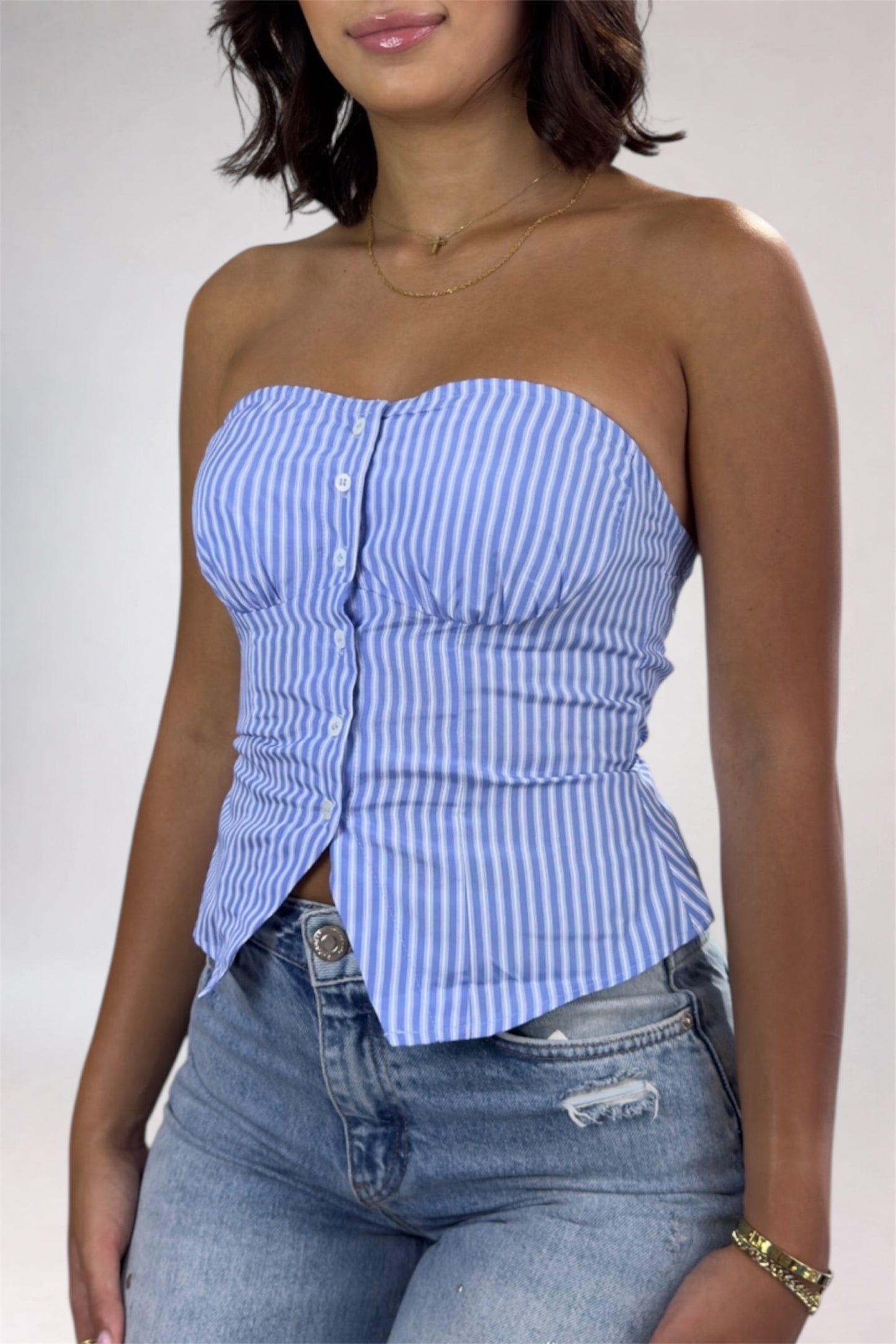 Woman wearing a blue and white striped strapless top and jeans on a plain background