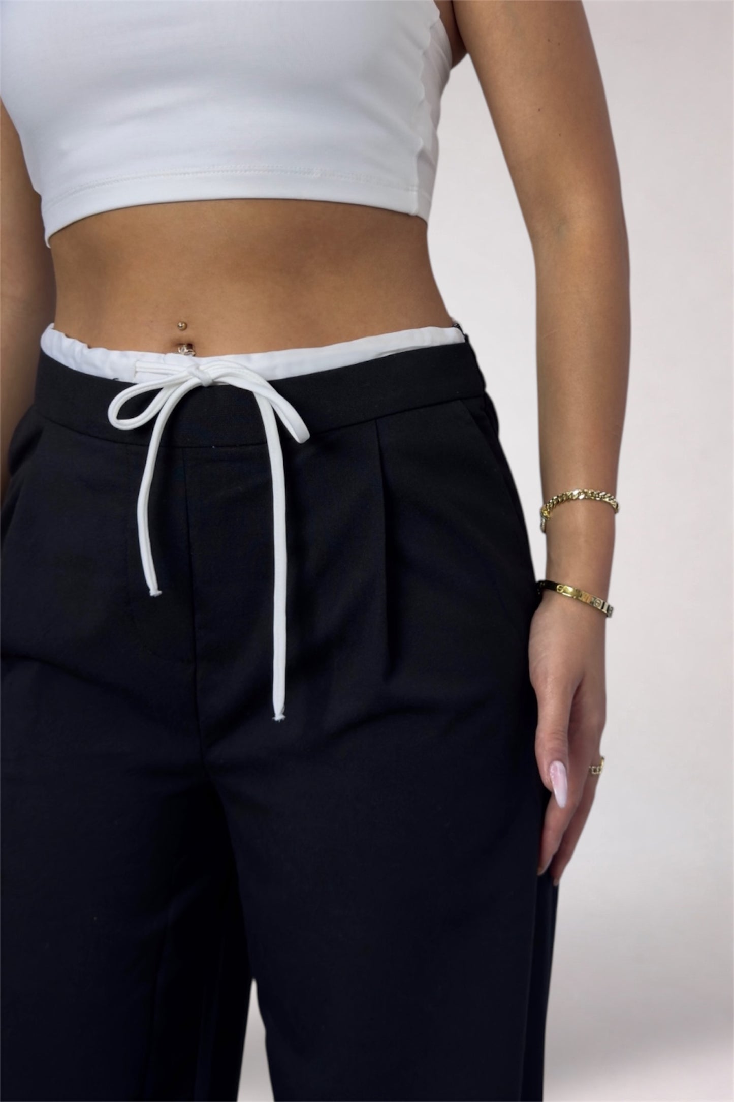 Person wearing black pants with a white drawstring and a white crop top on a light background