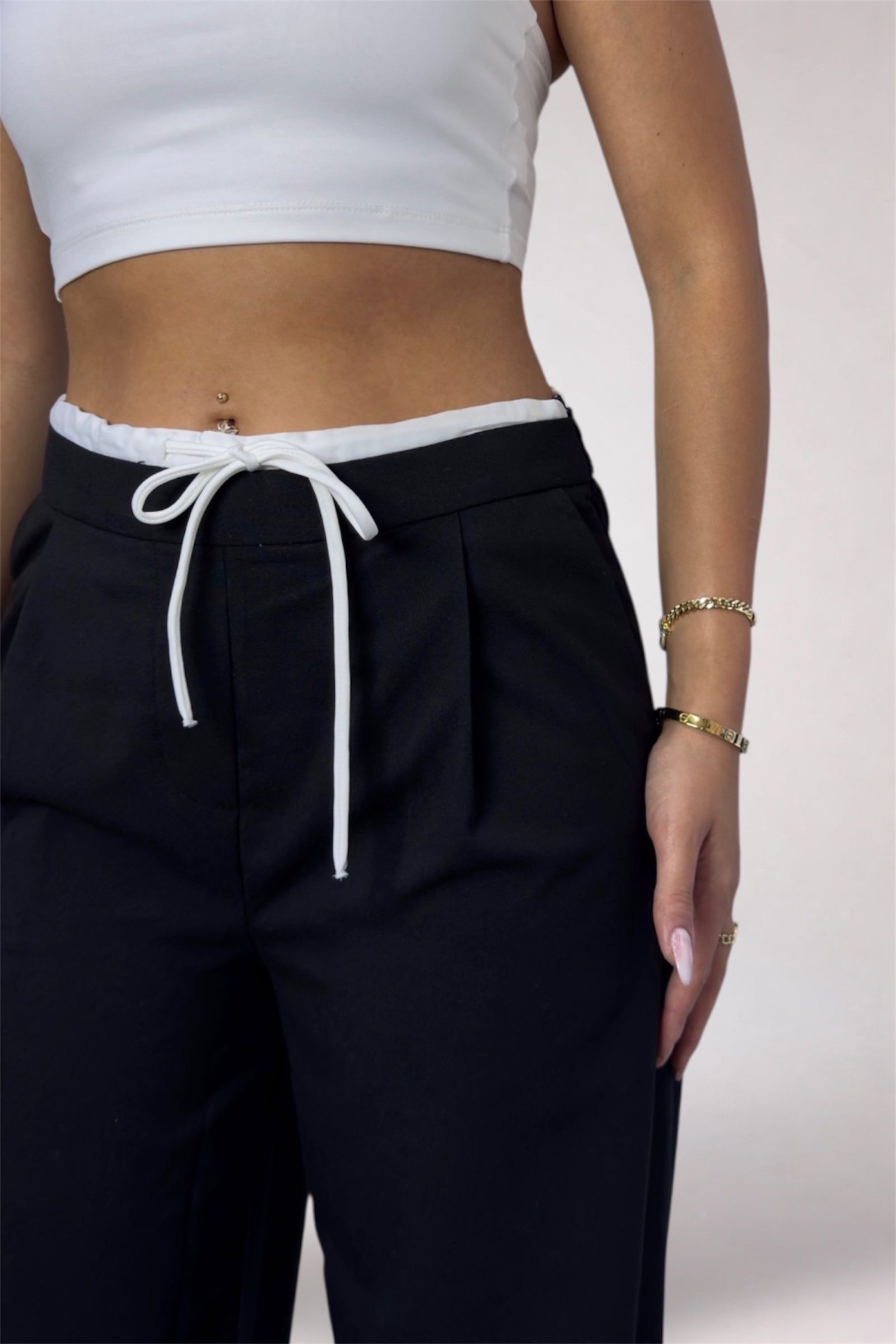 Person wearing black pants with a white drawstring and a white crop top on a light background