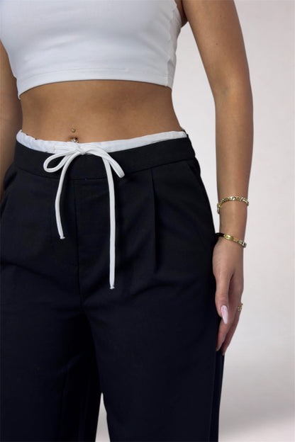 Person wearing black pants with a white drawstring and a white crop top on a light background