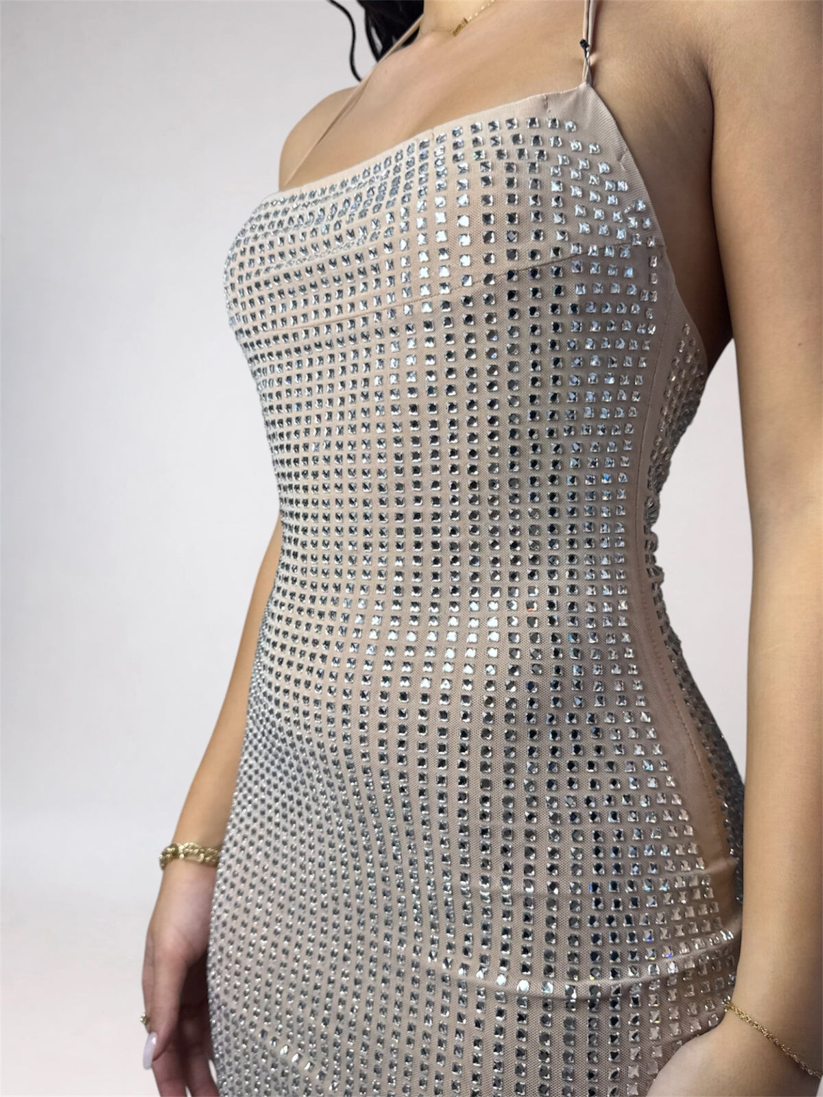 A woman modeling a sleeveless, bodycon mini dress covered in shimmering sequins. The dress has thin straps and a fitted silhouette, shown in a light beige/champagne color.