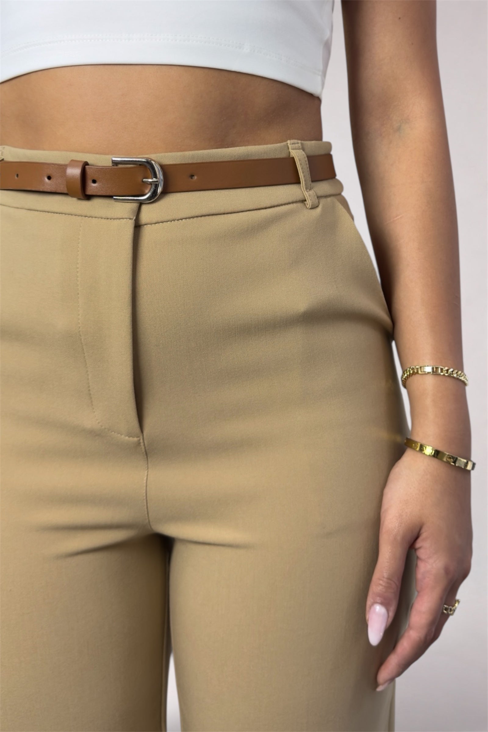 Beige pants with a brown belt worn by a person on a plain background