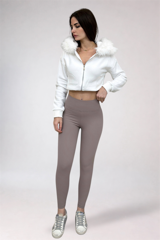 Woman wearing a white jacket with fur trim and gray leggings on a white background