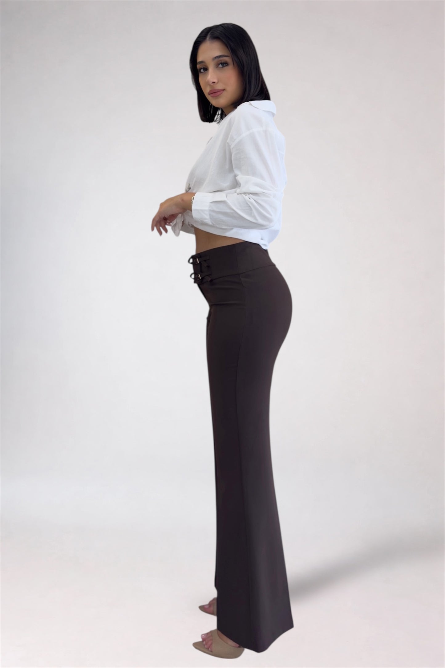 Woman wearing a white blouse and dark high-waisted pants on a white background