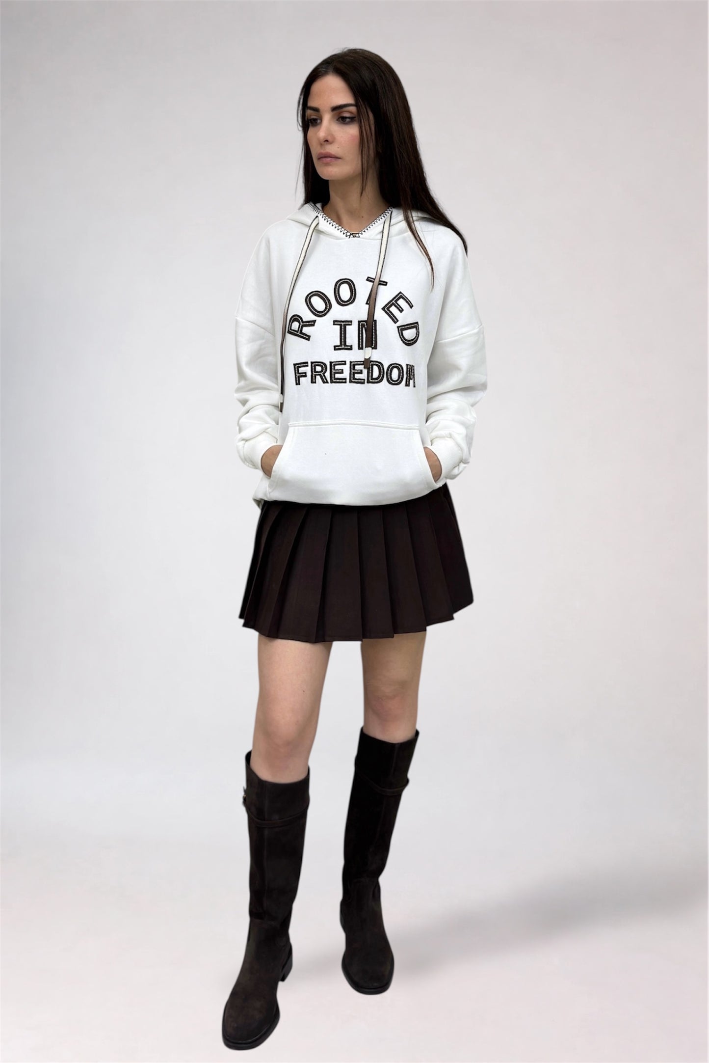 Person wearing a white hoodie with text, black skirt, and black boots on a white background