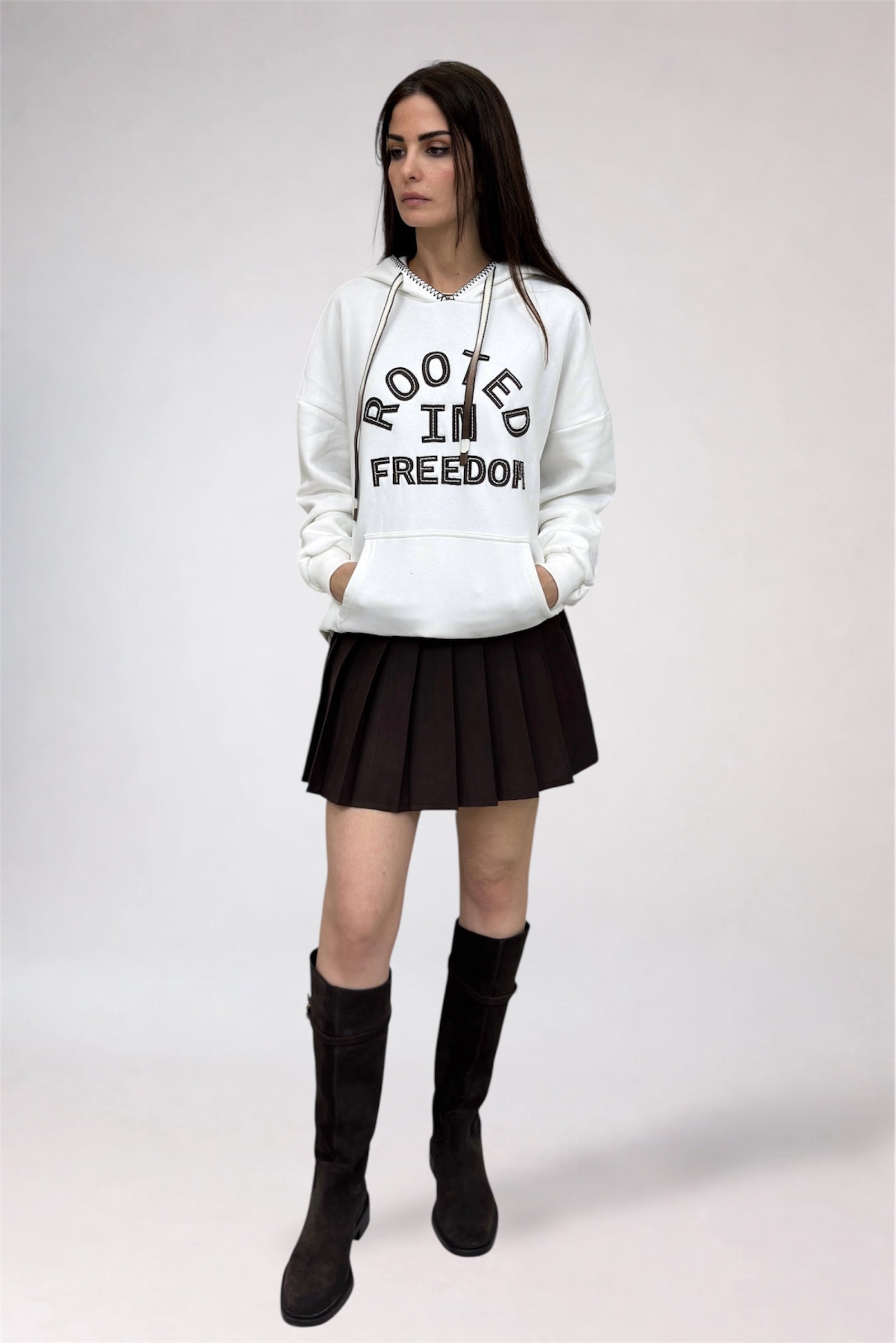 Person wearing a white hoodie with text, black skirt, and black boots on a white background