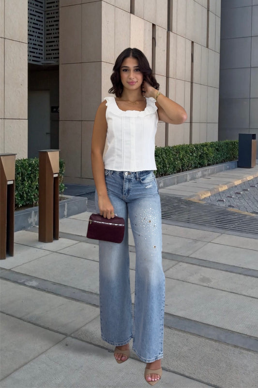 Woman in white top and blue jeans standing on a sidewalk with a building in the background