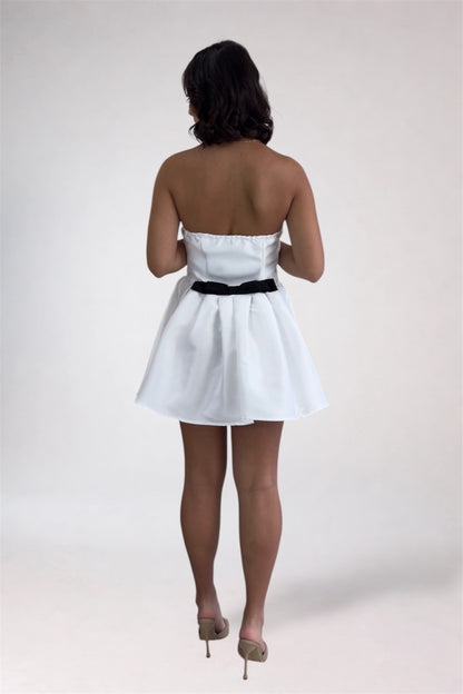 Woman wearing a white strapless dress with a black belt on a plain background