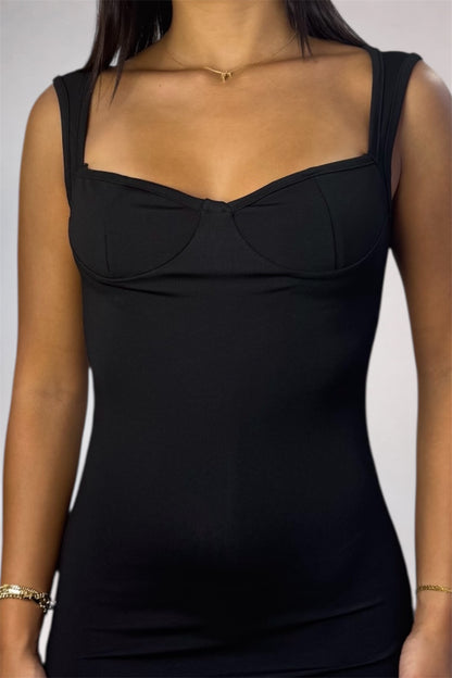 A close-up of a model wearing a black sleeveless bodysuit or shapewear top with a sweetheart neckline and structured bust cups, shown against a light gray background.