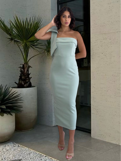 Woman in a light blue strapless dress standing outdoors next to a plant.
