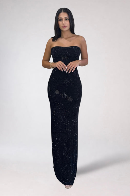 A woman modeling a strapless black sequined maxi dress against a plain light gray studio background.