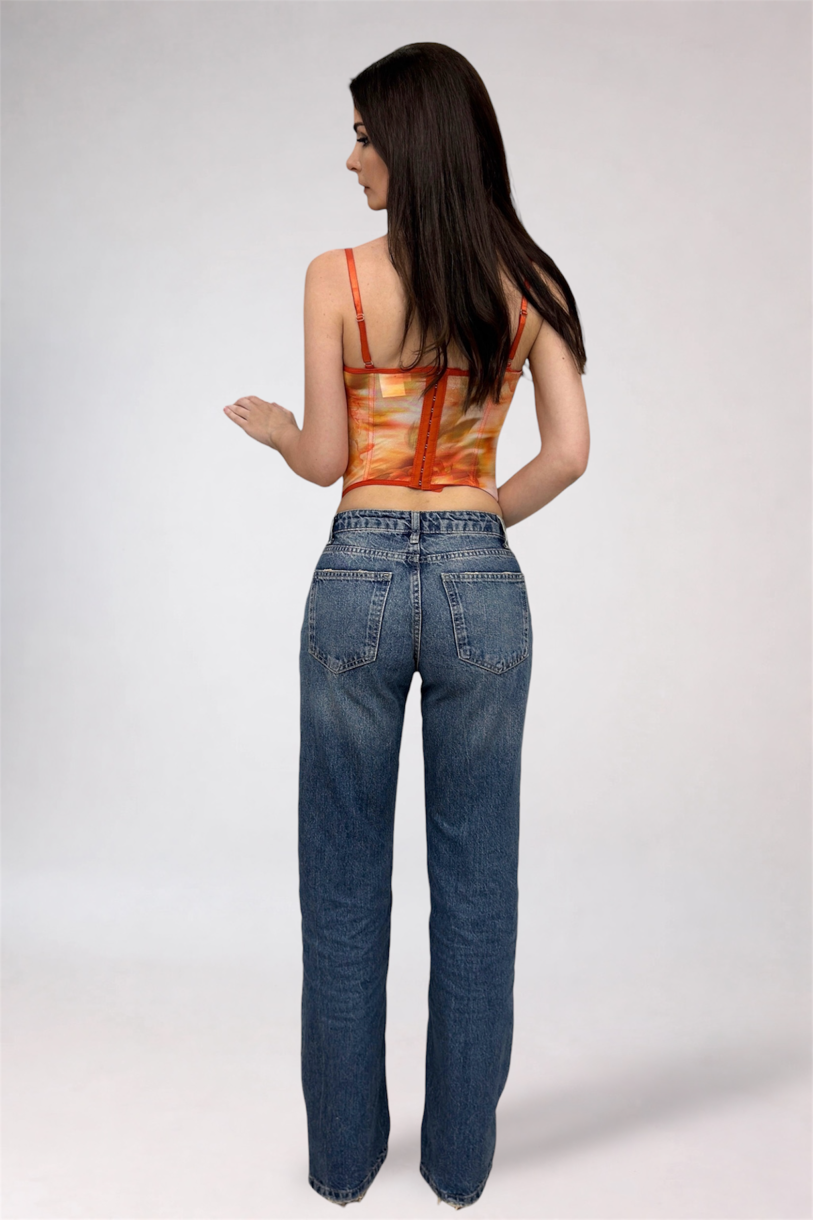 Woman wearing an orange top and blue jeans on a white background
