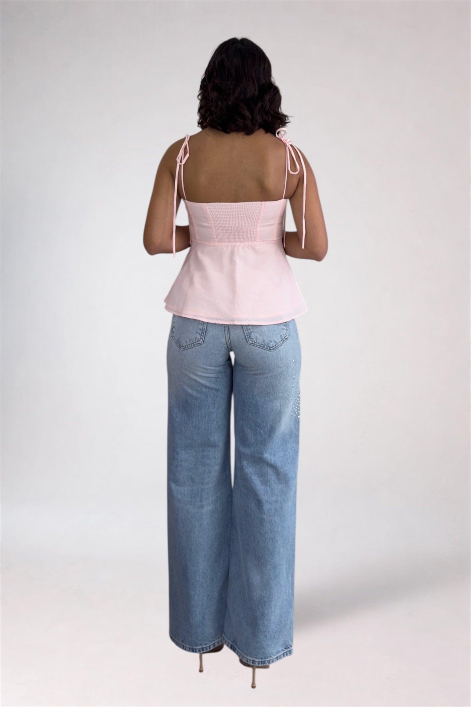 Person wearing a pink top and blue jeans on a white background