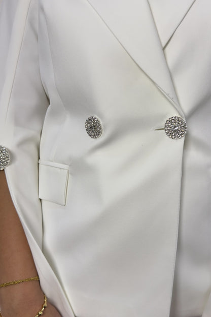 Close-up of a white blazer with decorative buttons and a gold bracelet.