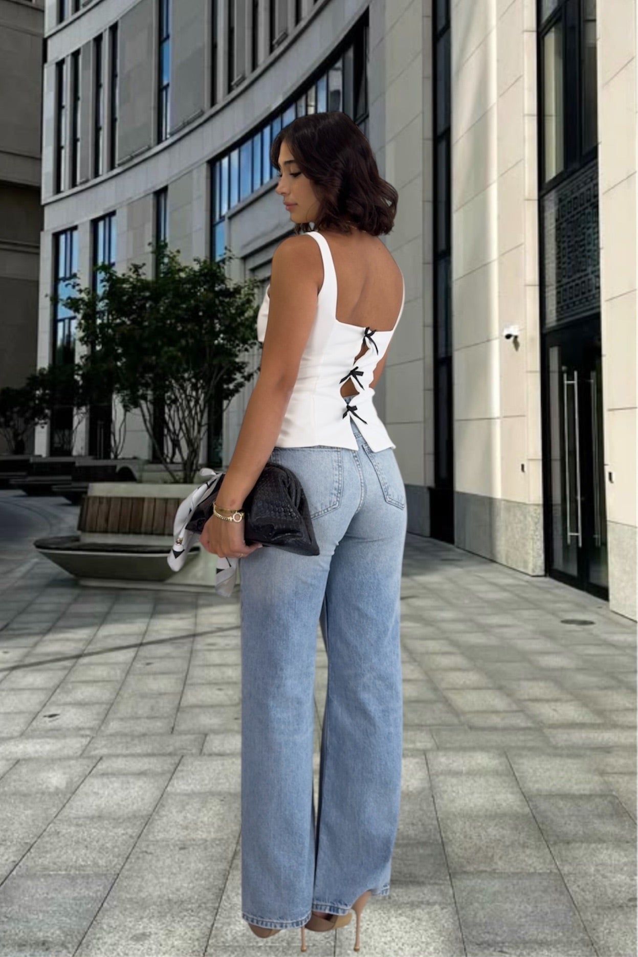 Woman in a white sleeveless top and blue jeans standing on a city street.