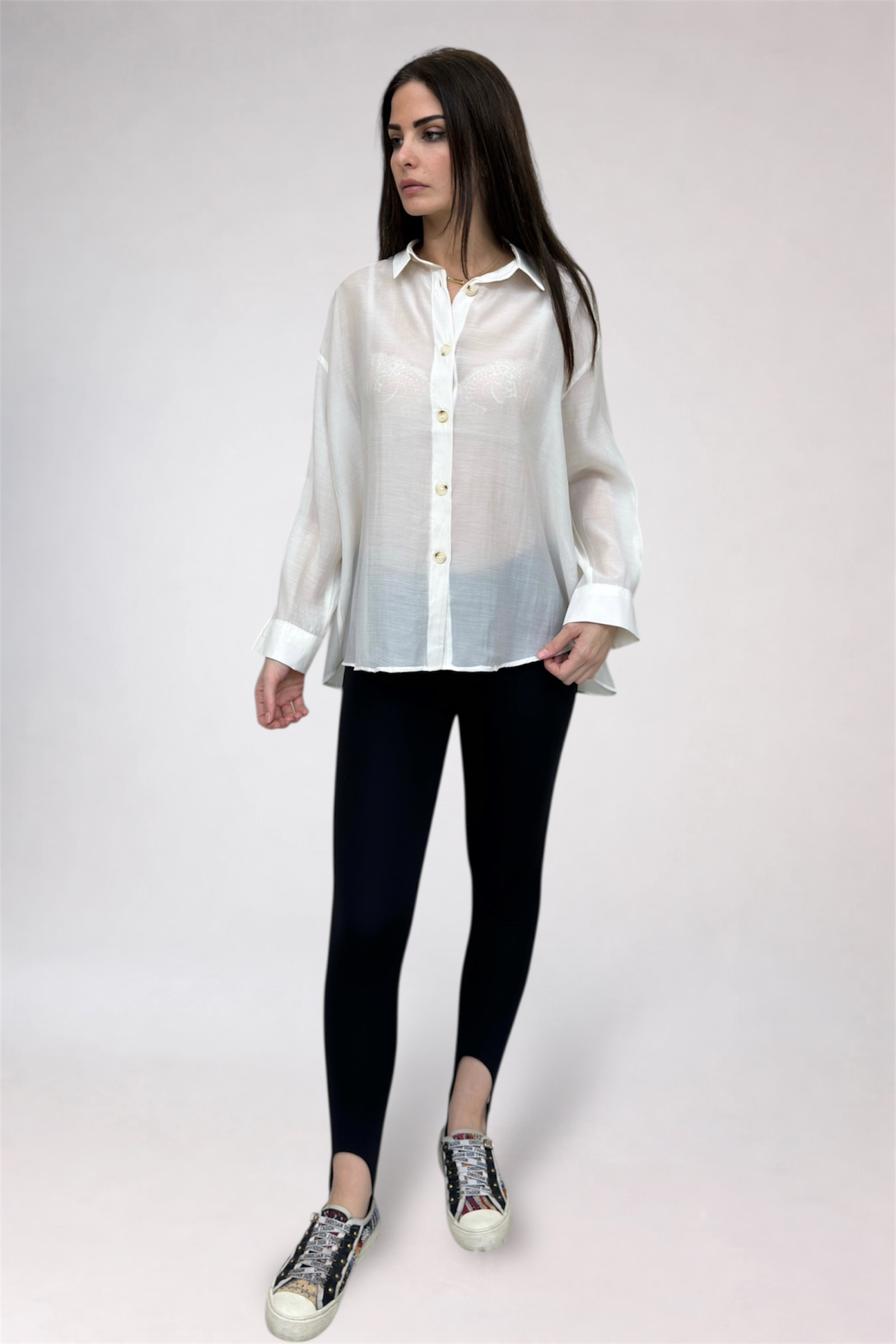 Woman wearing a white shirt, black leggings, and patterned shoes on a plain background