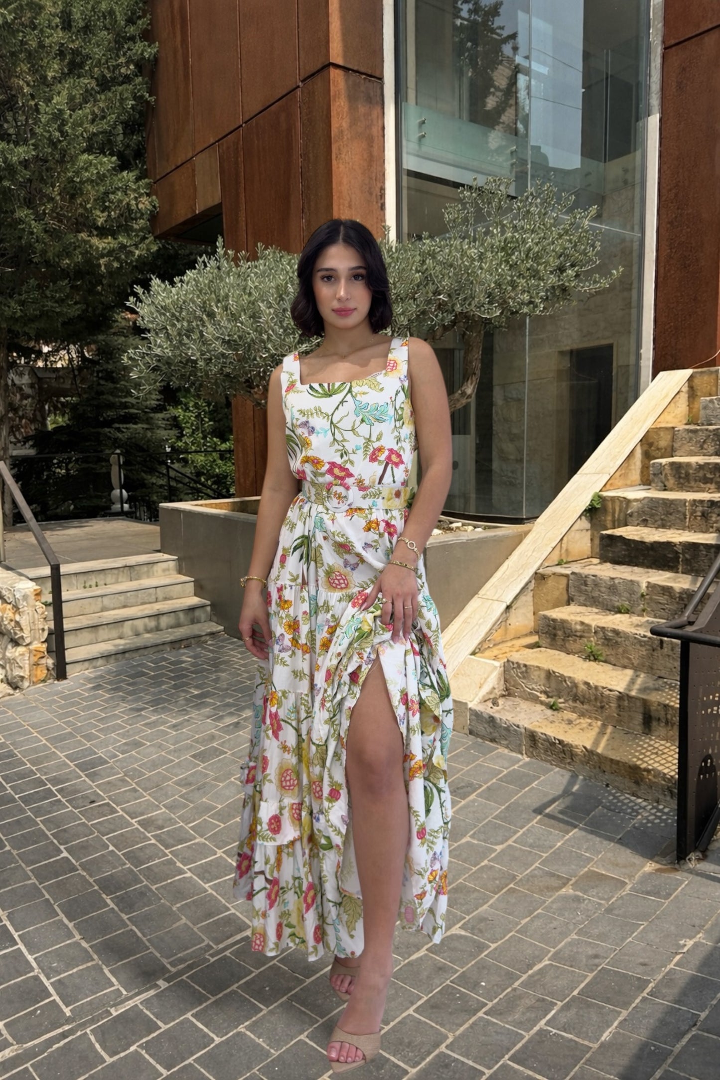Woman in a floral dress standing on a sidewalk with a building in the background