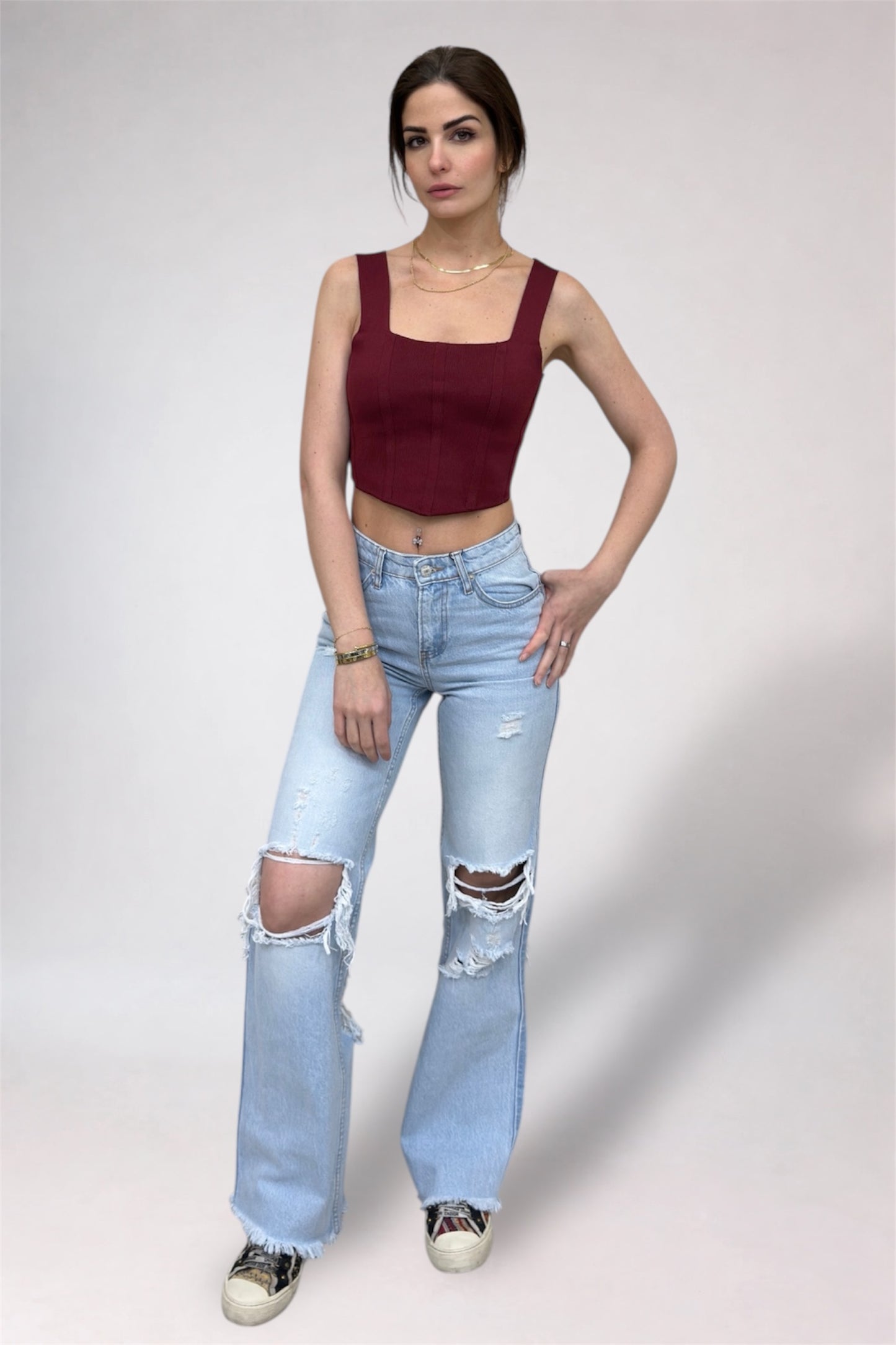 Woman wearing a burgundy top and light blue ripped jeans on a plain background