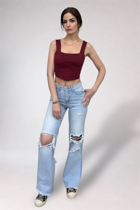 Woman wearing a burgundy top and light blue ripped jeans on a plain background