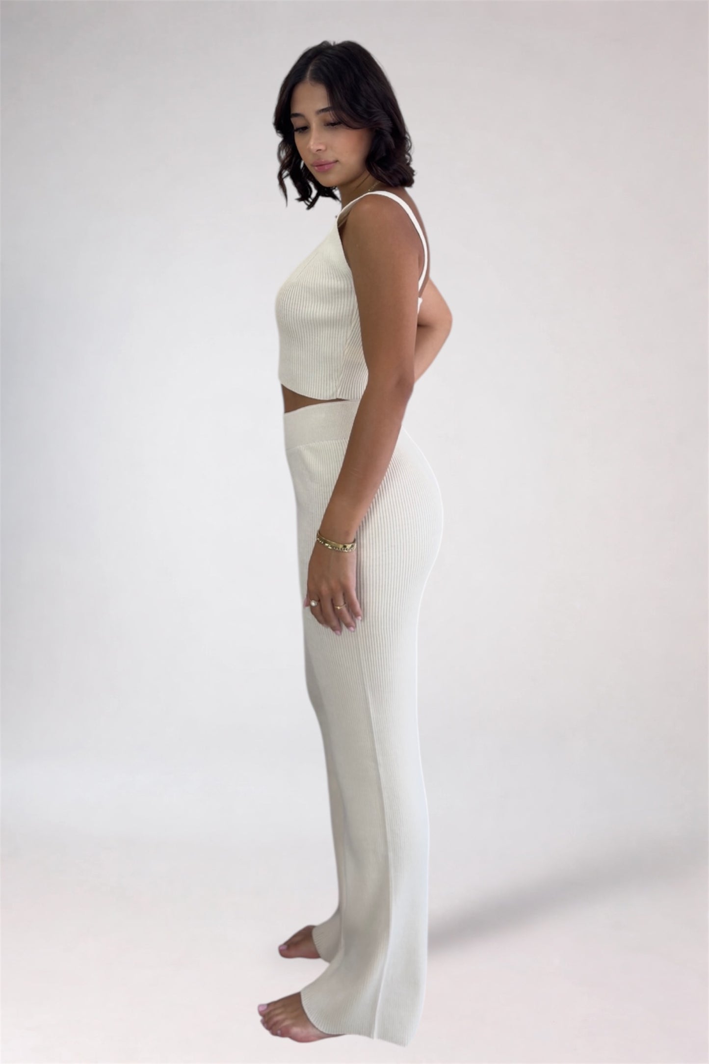 Woman wearing a white sleeveless top and pants on a plain background