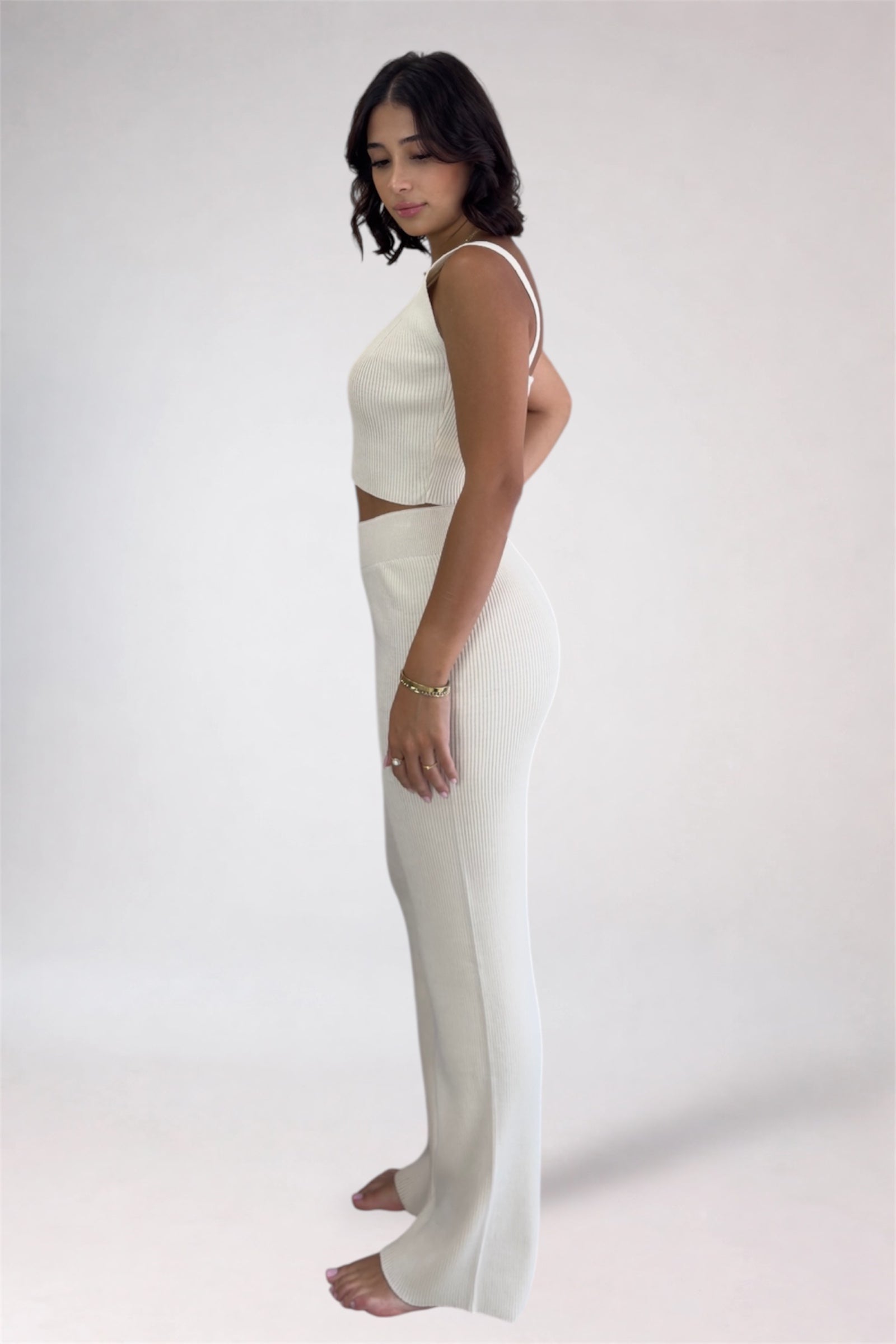 Woman wearing a white sleeveless top and pants on a plain background