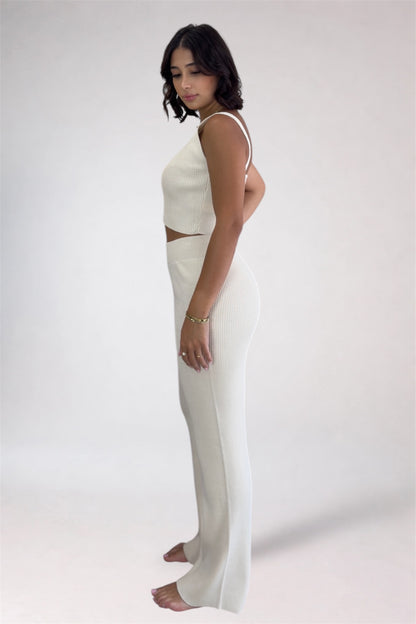 Woman wearing a white sleeveless top and pants on a plain background