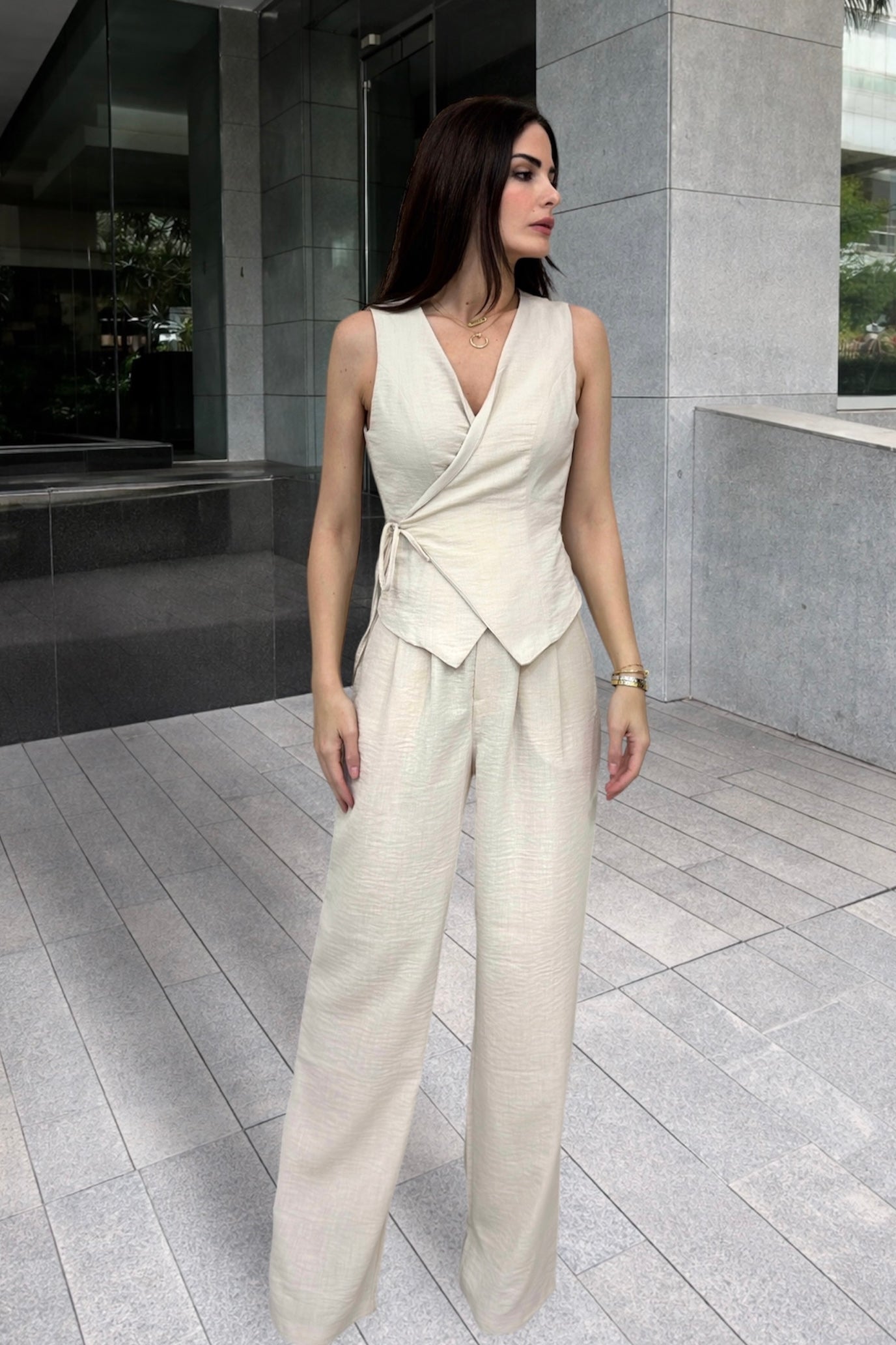 Woman wearing a white sleeveless top and wide-leg pants standing in an urban setting.