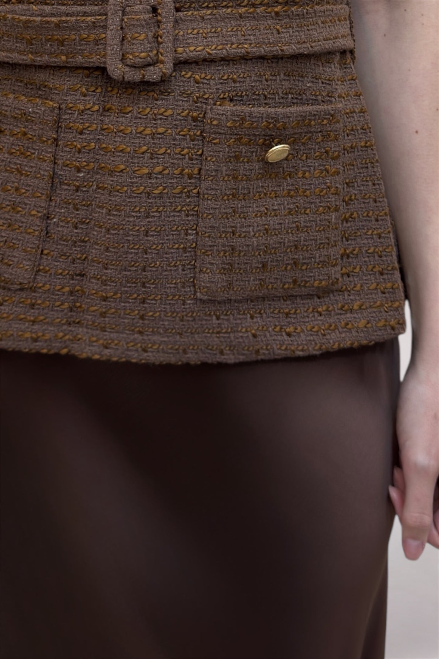 Brown textured jacket with a belt and button on a plain background