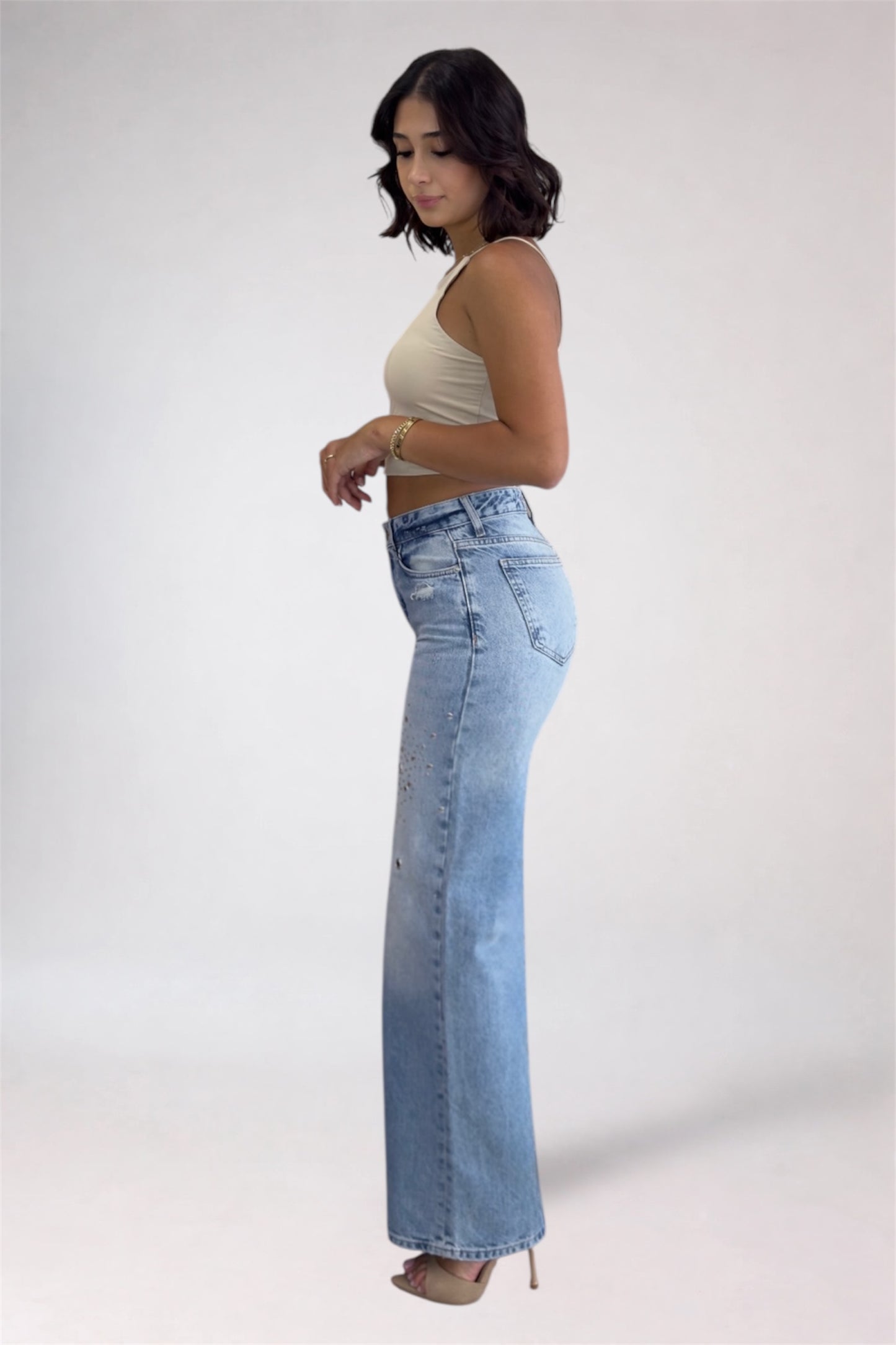 Woman wearing light blue jeans and a beige top on a white background