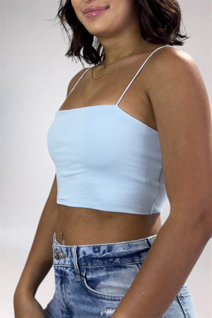 Woman wearing a light blue crop top and blue jeans against a plain background