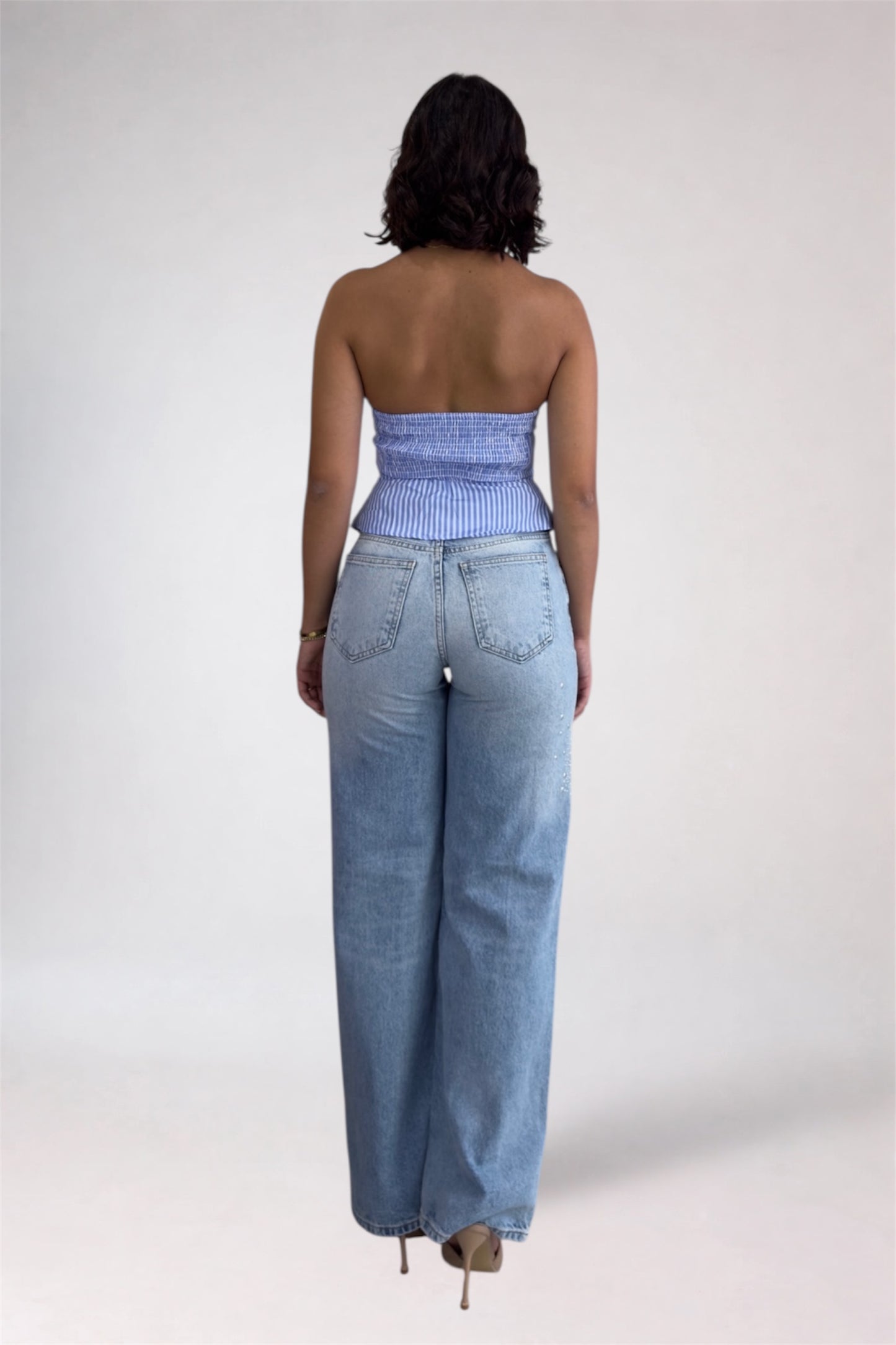 Person wearing a strapless top and high-waisted jeans on a plain background