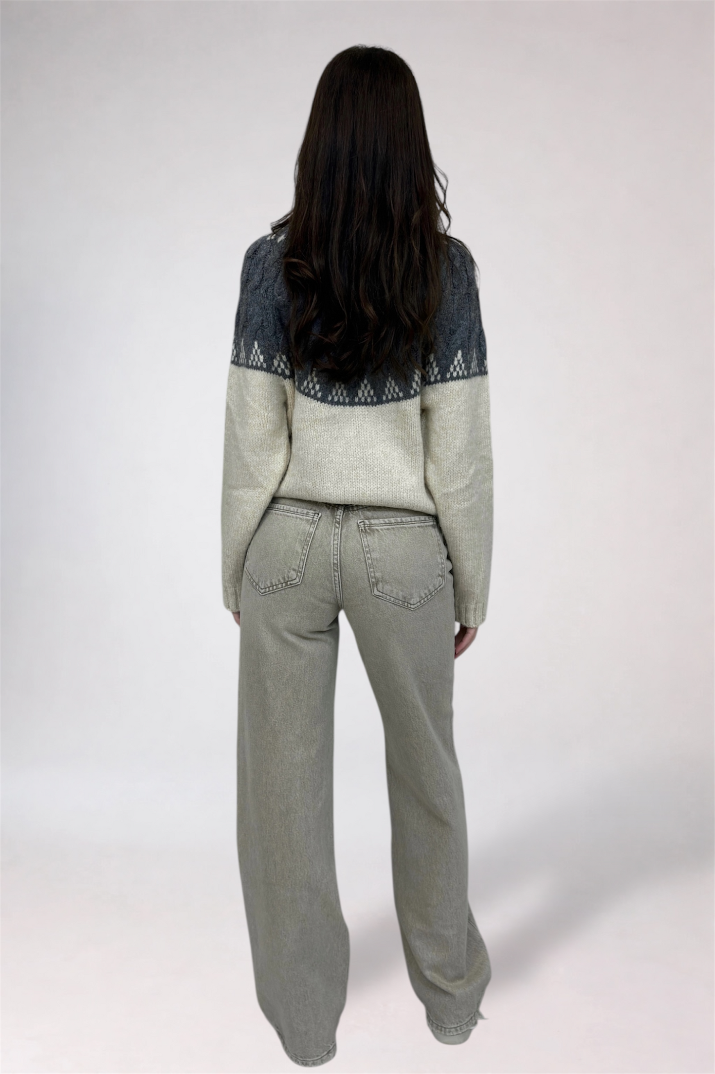 Person wearing a patterned sweater and light-colored pants on a white background