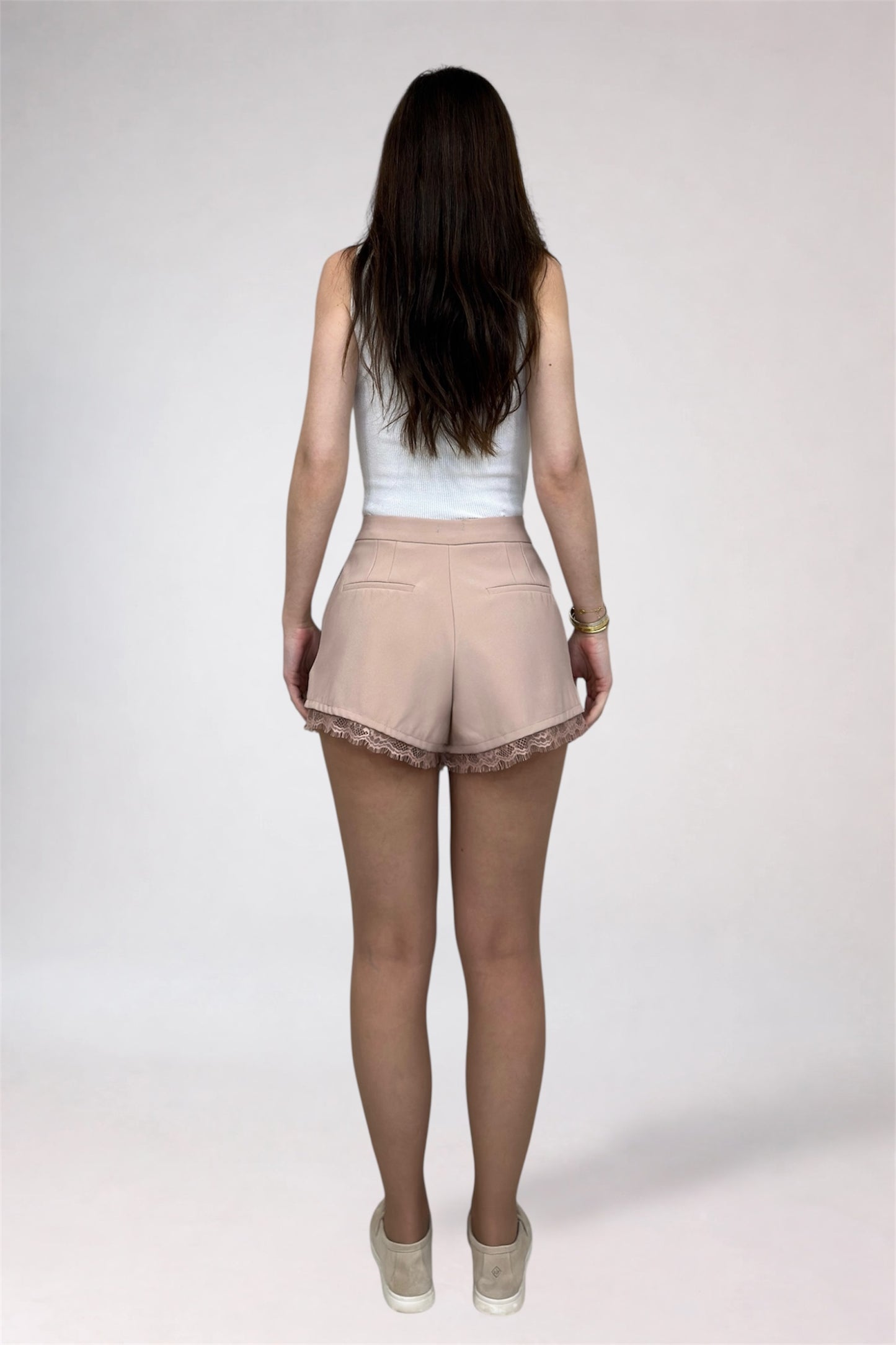 Woman wearing a white top and beige shorts on a plain background
