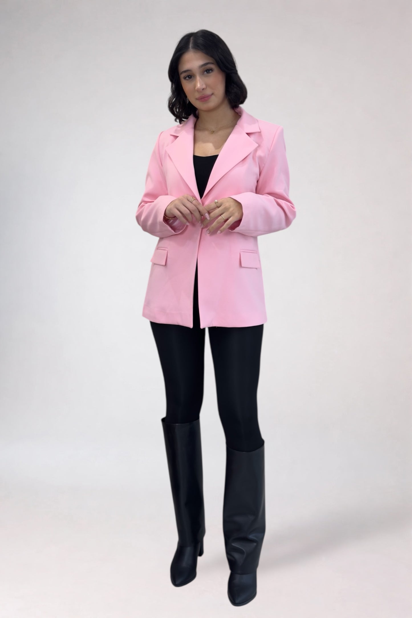 Person wearing a pink blazer, black top, leggings, and black boots on a white background