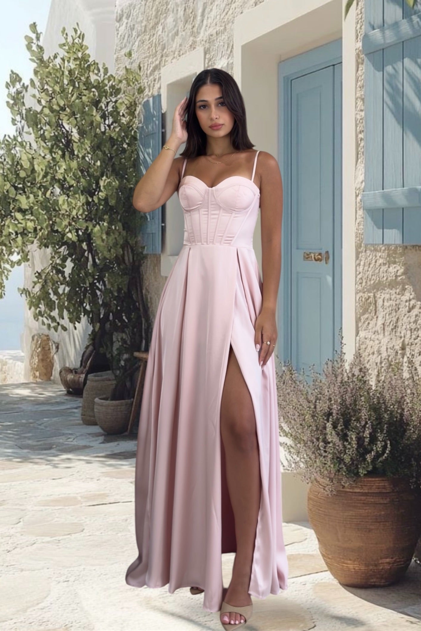 Woman in a pink dress standing outdoors with a building and plants in the background