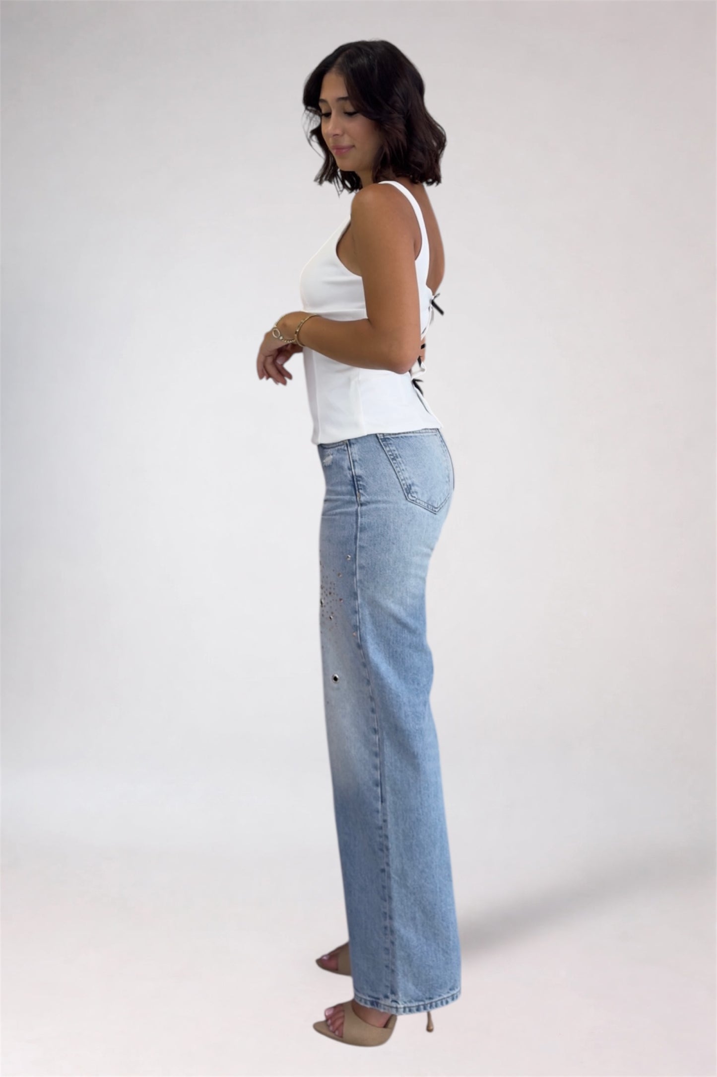 Woman wearing a white tank top and blue jeans on a plain background