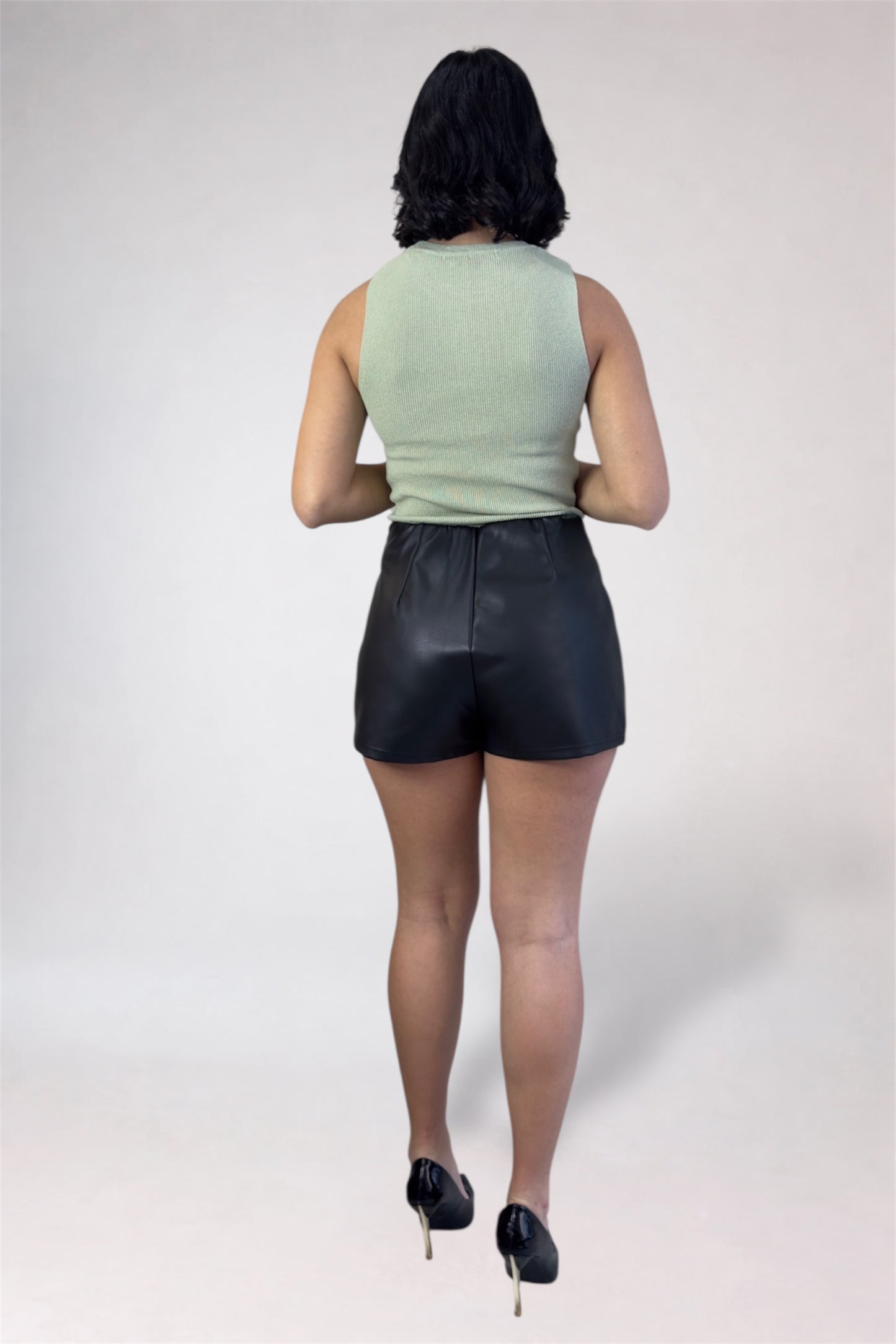 Person wearing a light green sleeveless top and black leather shorts on a white background
