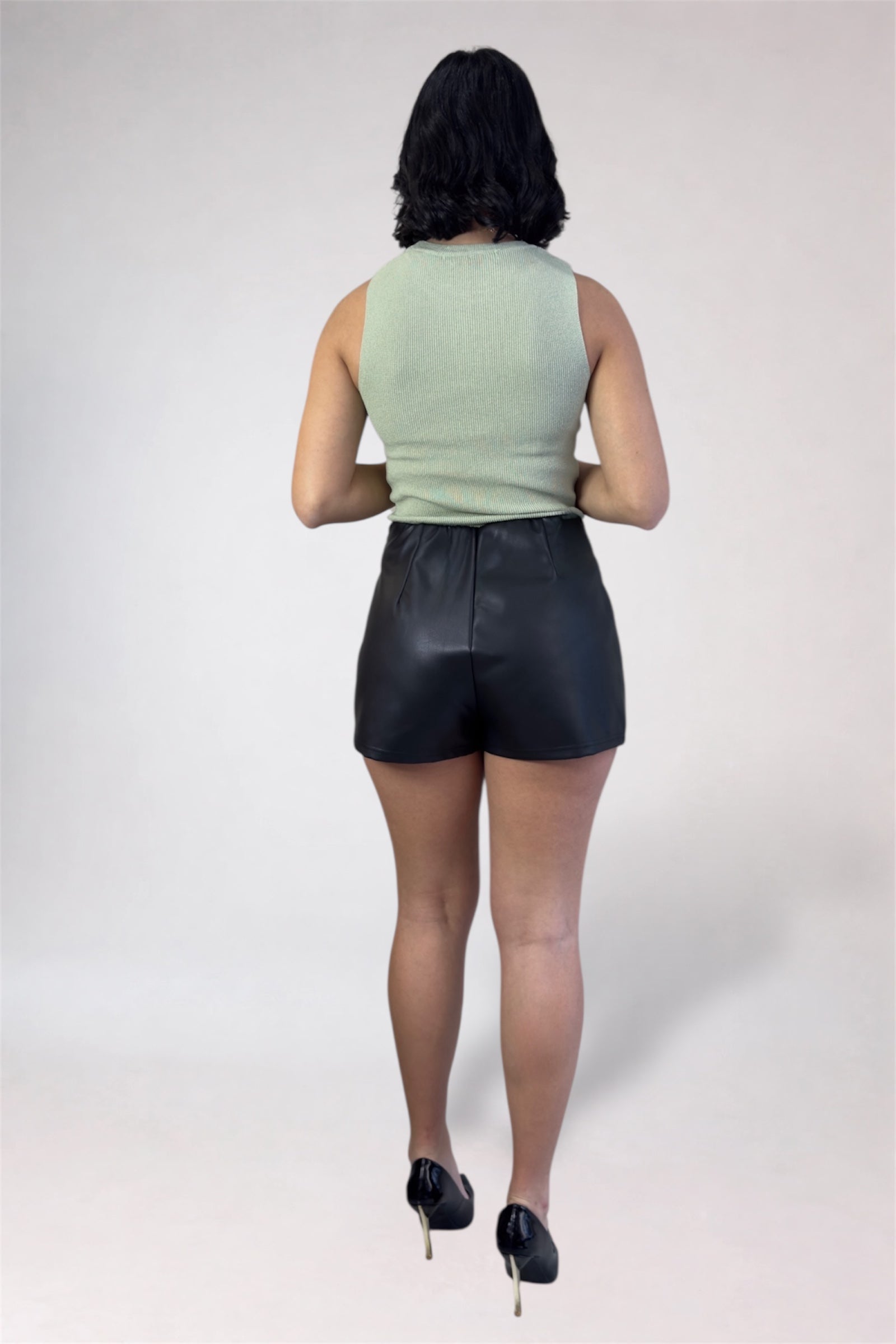 Person wearing a light green sleeveless top and black leather shorts on a white background
