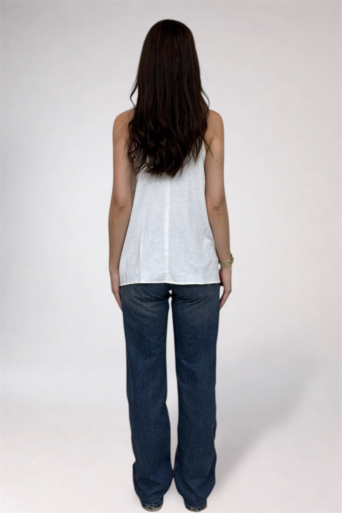 Person wearing a white sleeveless top and dark blue jeans on a white background